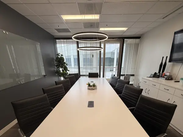 The firm's conference room, a long white table with black leather chairs under two ring pendant lights, with a window along one side.