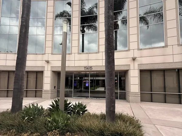 The entrance to 15615 Alton Parkway, a pale stone office building with the street number above glass doors, framed by two palm trees.