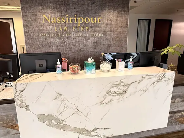 The firm's reception desk, a white marble counter in front of a textured wall carrying Nassiripour Law Firm, Immigration and Appellate Litigation in gold letters.