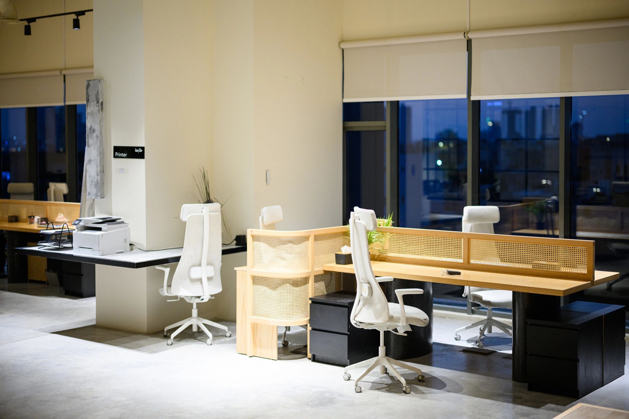 Wide shot of empty contemporary coworking office interior with shared desks, ergonomic chairs and city view at night